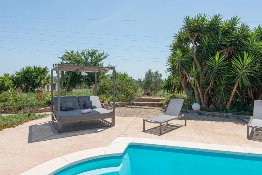 A swimming pool beside a paved patio with outdoor seating and leafy plants.