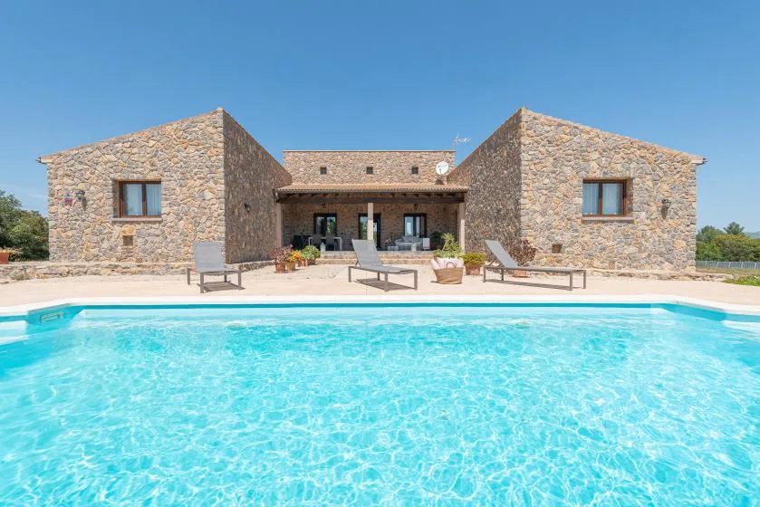 A swimming pool in front of a stone house with outdoor seating.