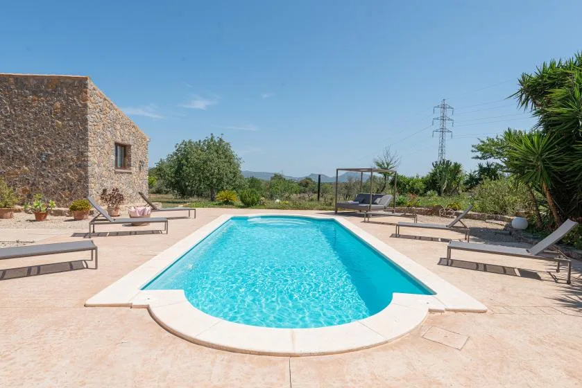 An outdoor swimming pool sits beside a stone building, with loungers around the patio.