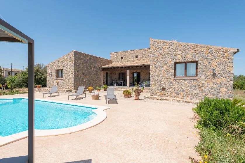 A stone house beside a curved swimming pool and sunny patio.