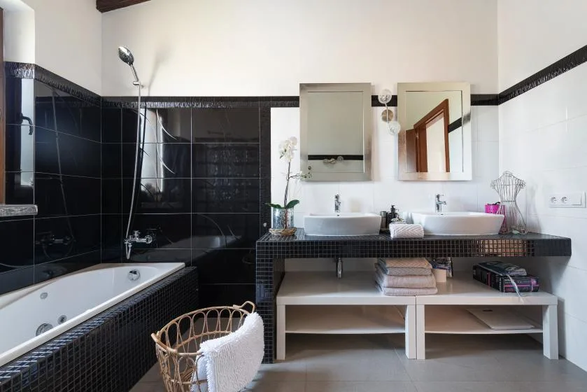 A bathroom with a bathtub, two sinks, and dark tiled walls.
