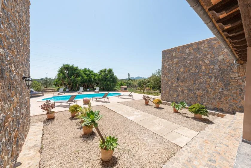 A sunny outdoor pool area with stone walls and potted plants.