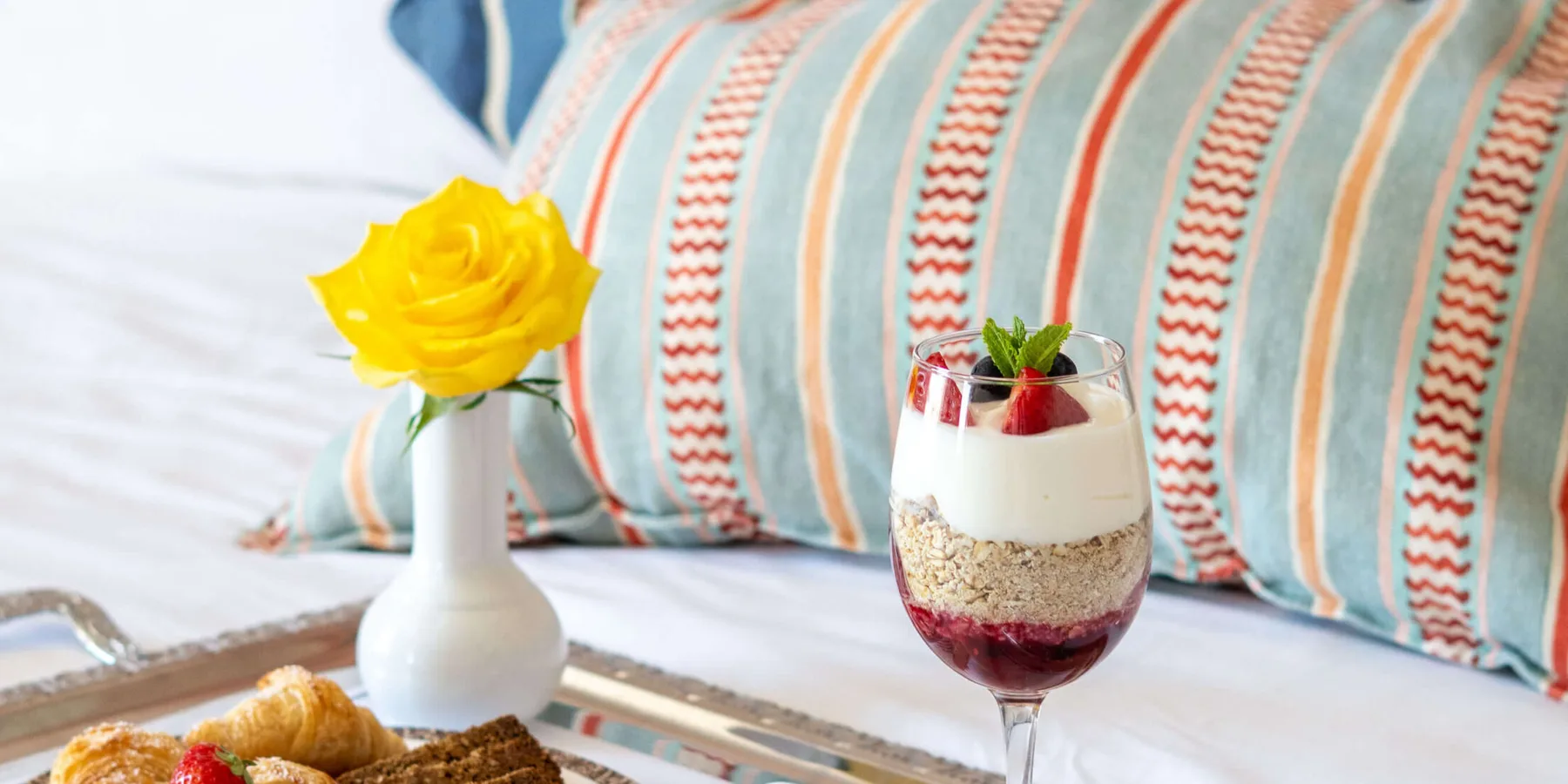 Bollería de desayuno y un parfait dispuestos sobre una cama de hotel.