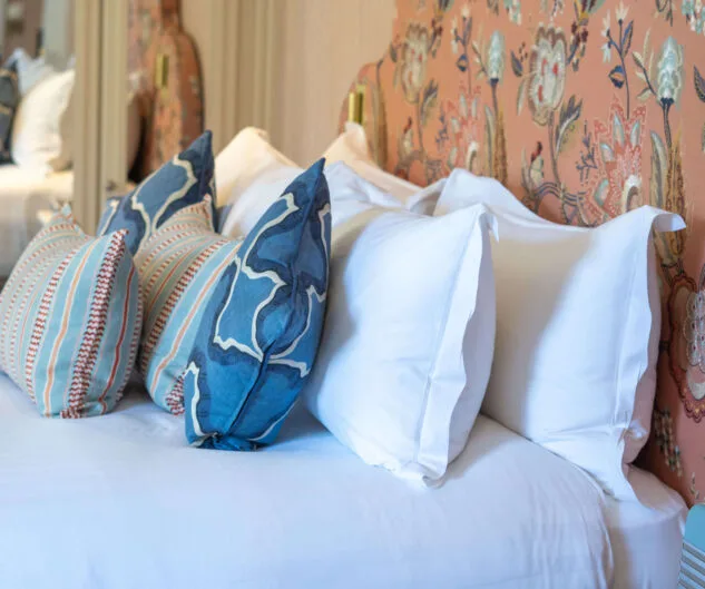 Cama de hotel con almohadas blancas y azules y un cabecero con estampado floral.