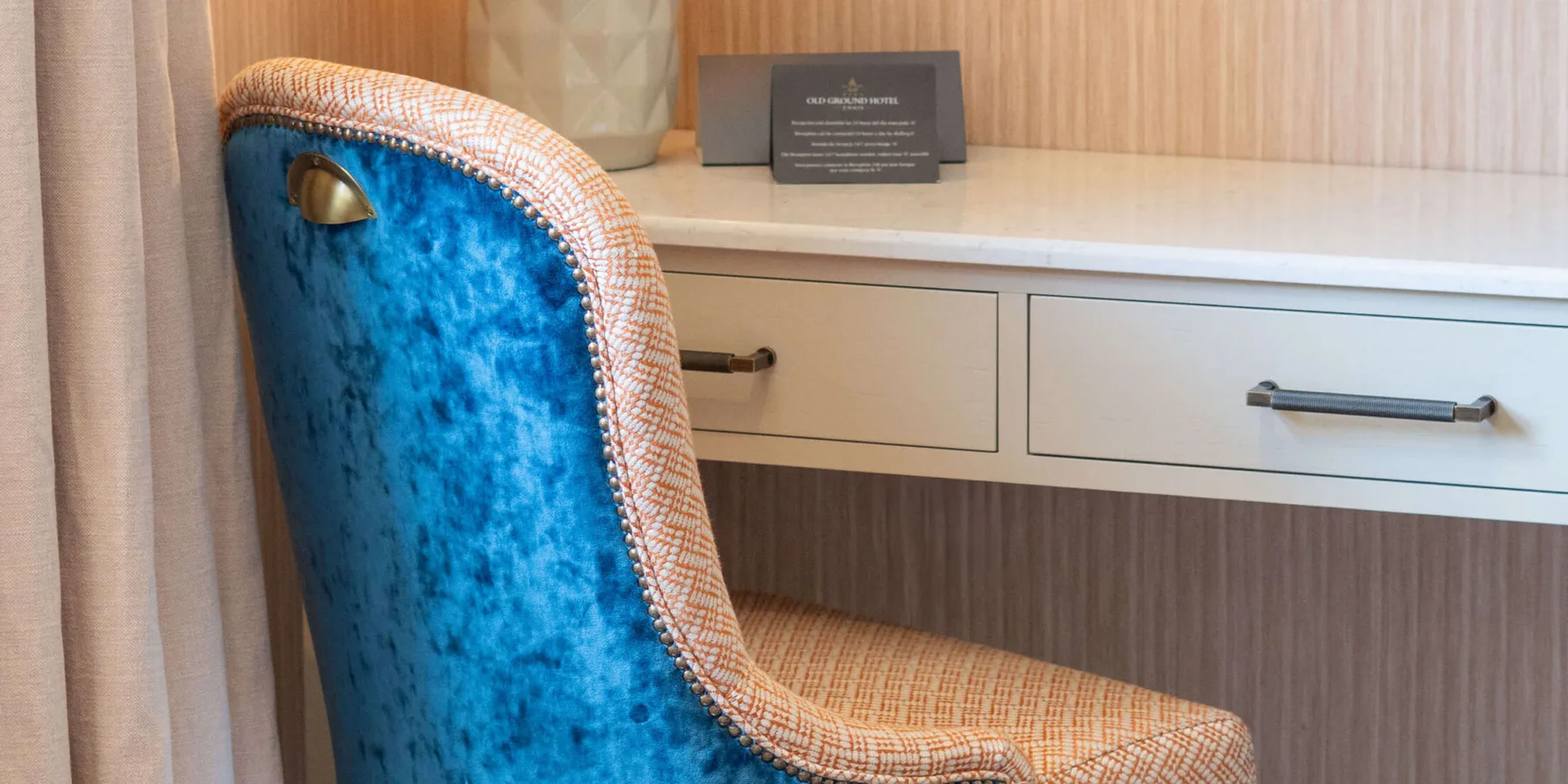 Habitación de hotel con una silla de terciopelo azul y una lámpara.