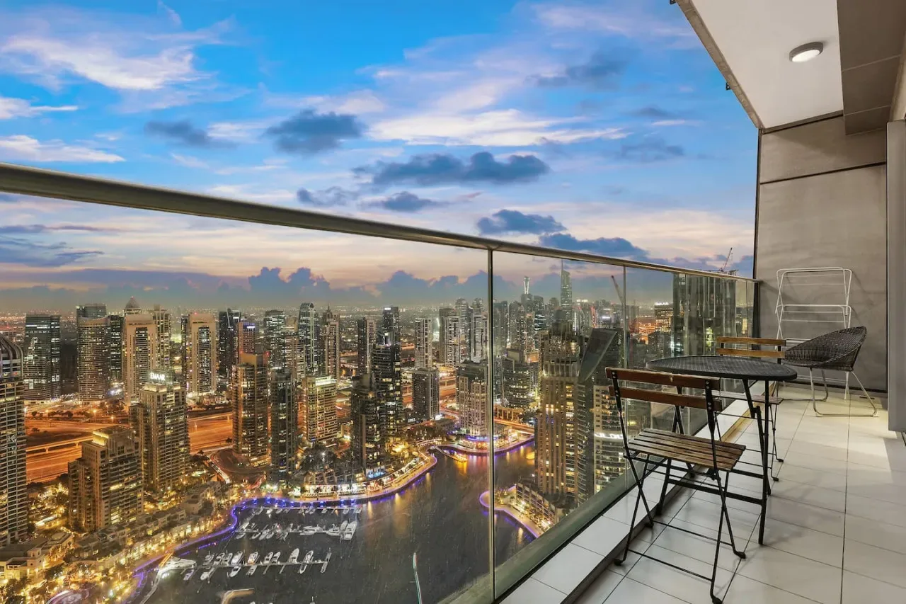 Un balcón elevado ofrece vistas de un horizonte urbano iluminado y la costa al anochecer.