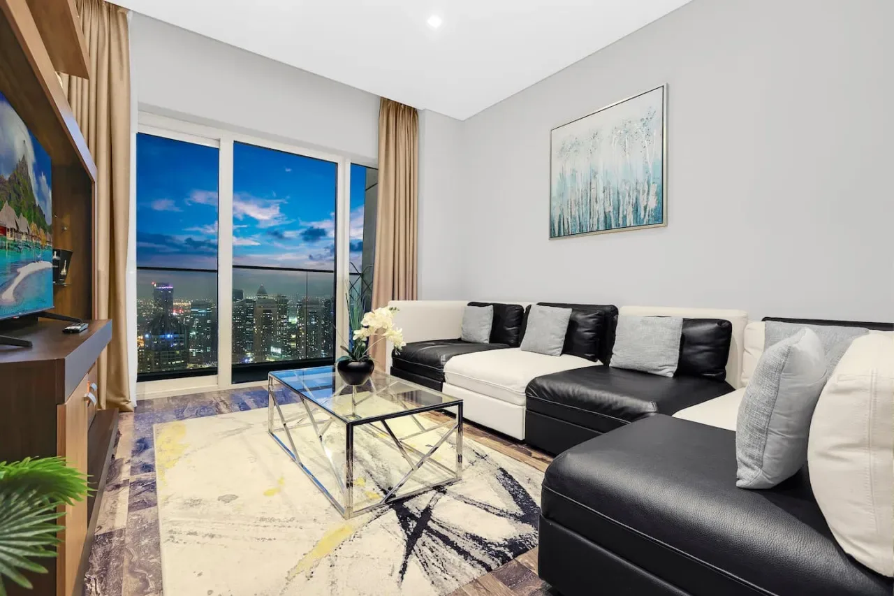 Una sala de estar moderna con asientos seccionales, una mesa de centro de vidrio y vistas de la ciudad por grandes ventanales.