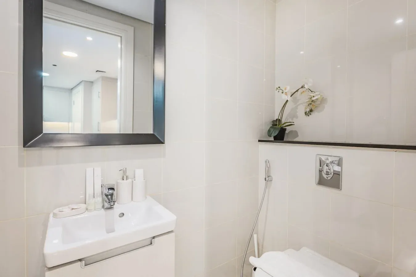Un baño luminoso con azulejos, lavabo, espejo y accesorios de ducha.