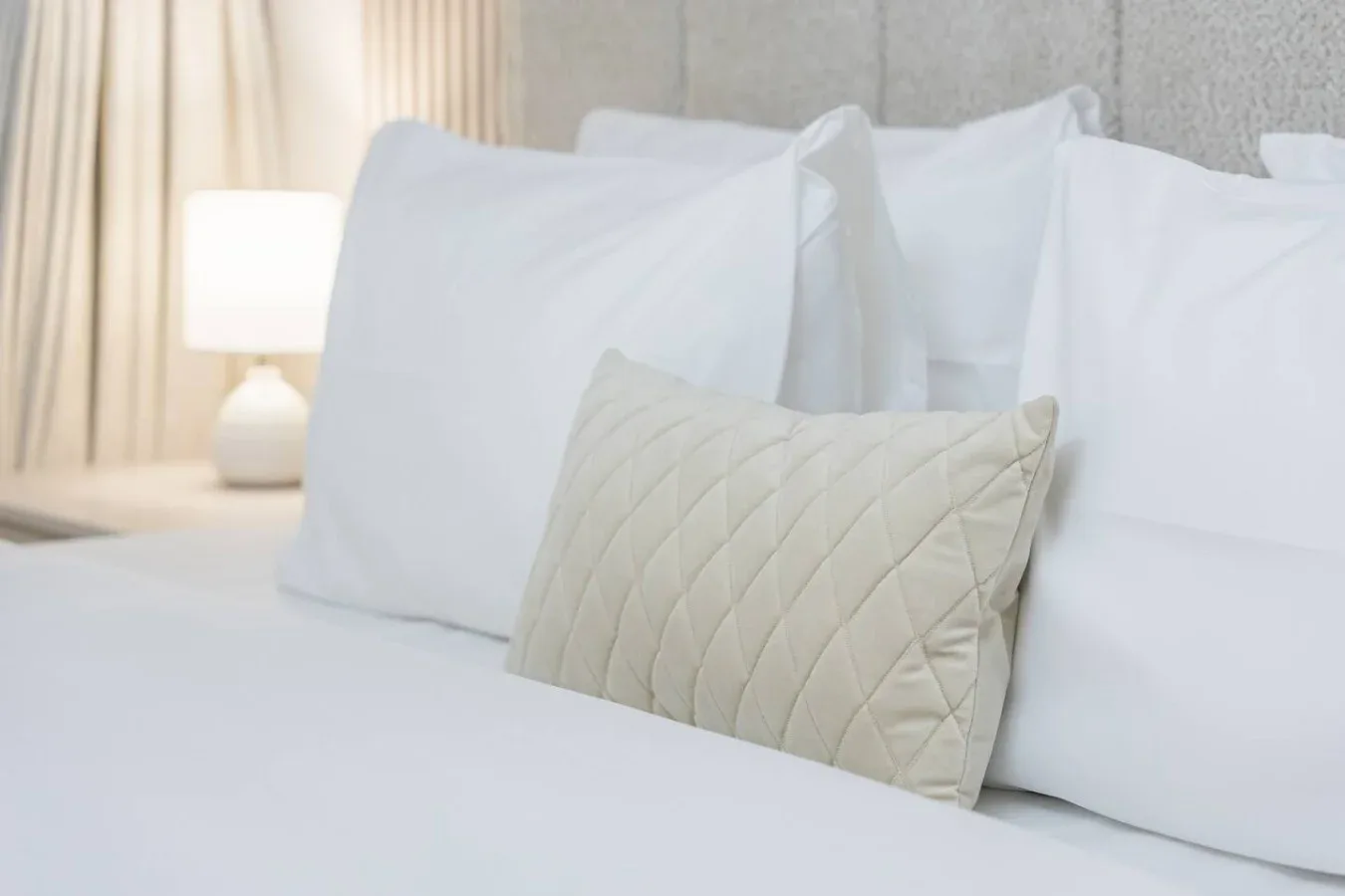Una cama de dormitorio está arreglada con almohadas blancas y un cojín acolchado.