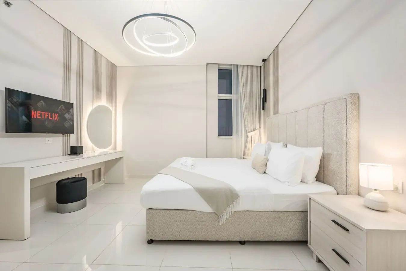 Un dormitorio luminoso cuenta con una cama, un televisor montado en la pared y un escritorio.