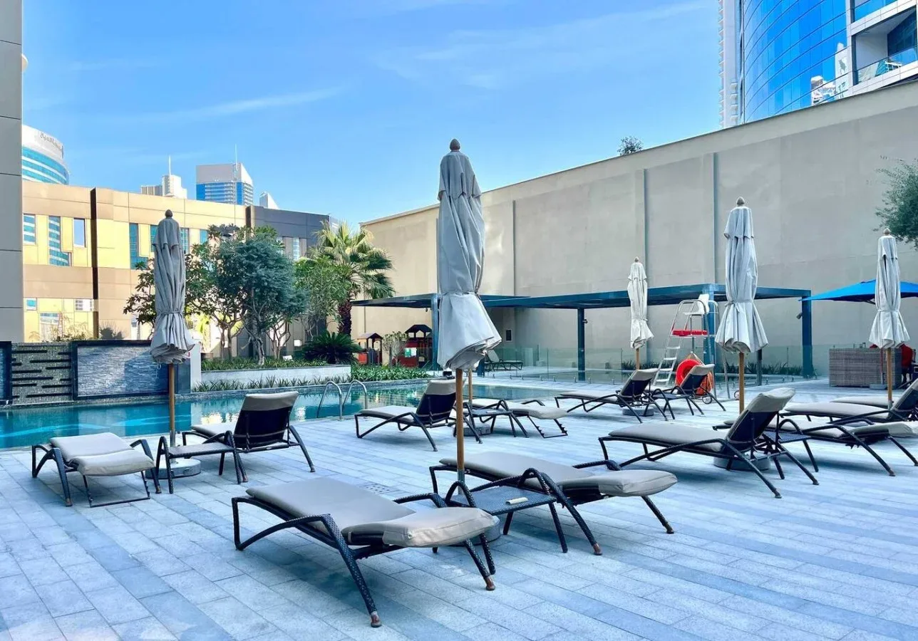 Una zona exterior junto a la piscina con tumbonas y sombrillas cerradas.