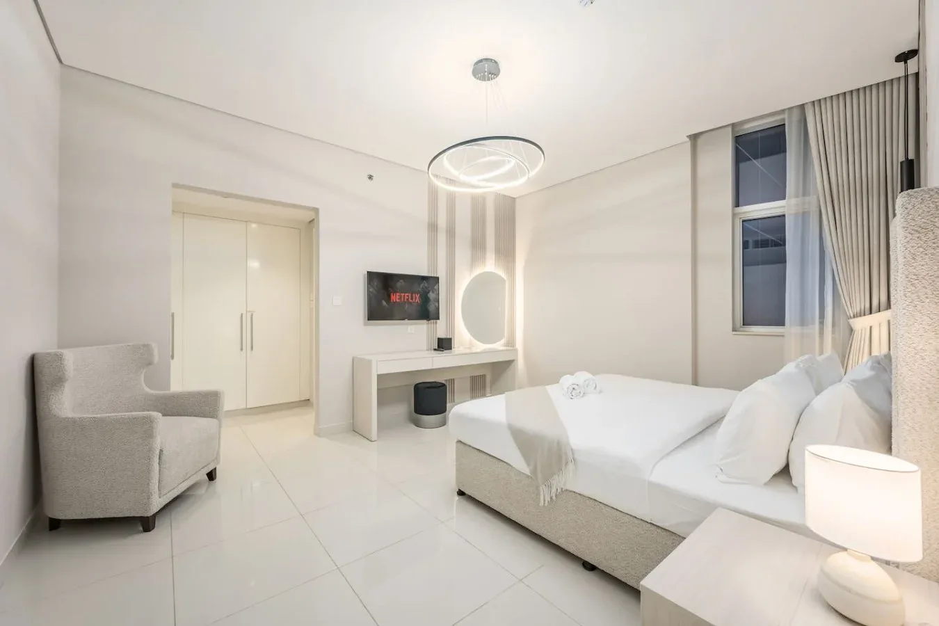 Un dormitorio luminoso con cama, sillón y televisor.