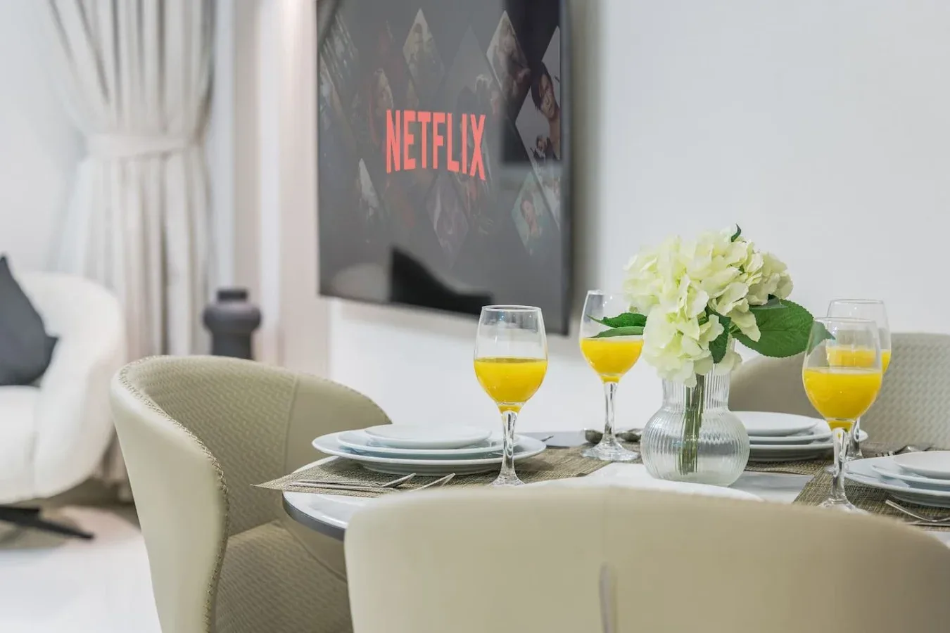 Una mesa está puesta con platos, bebidas y flores frente a un televisor.