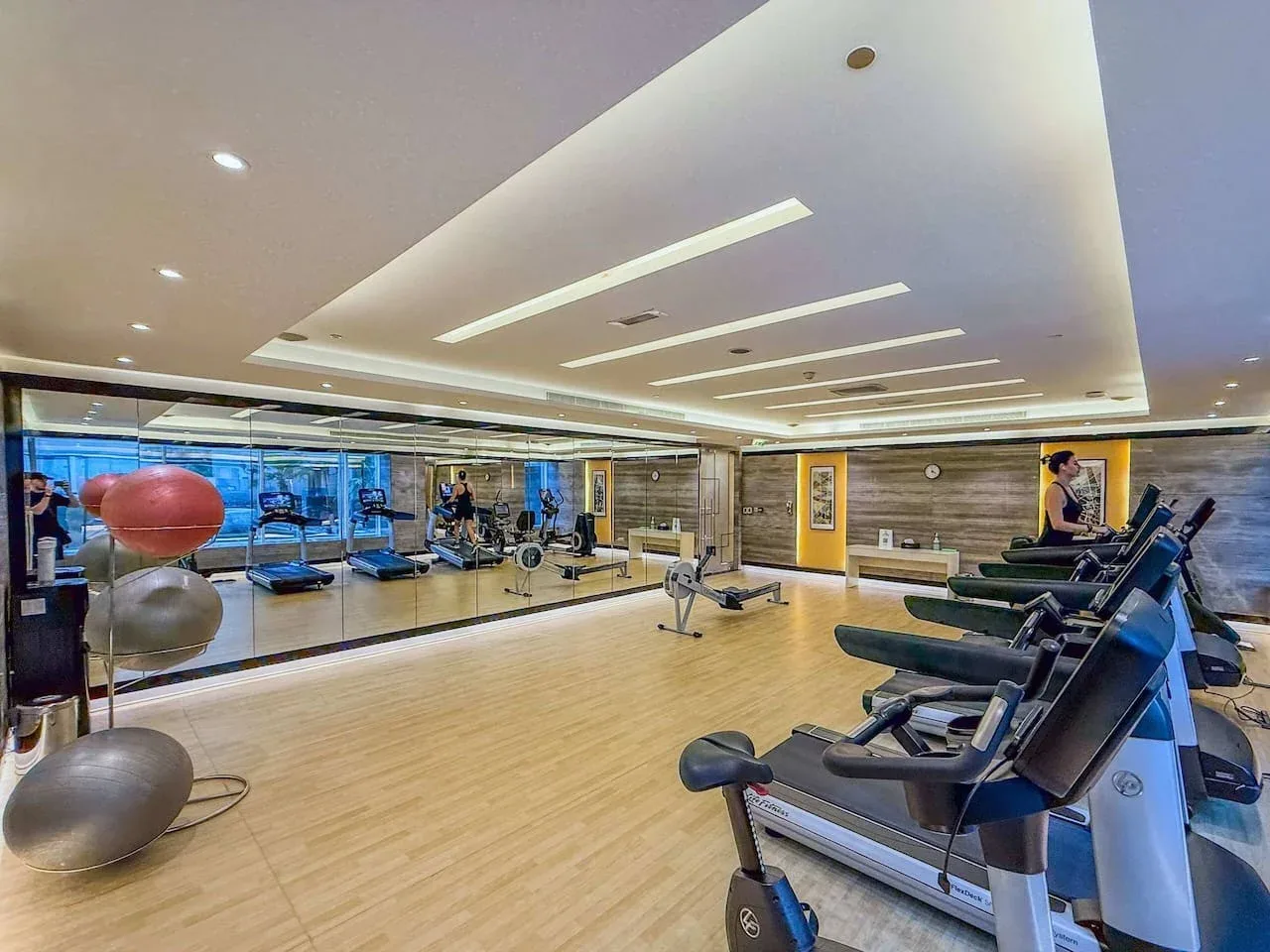 Un gimnasio con aparatos de ejercicio, cintas de correr y una pared con espejos.