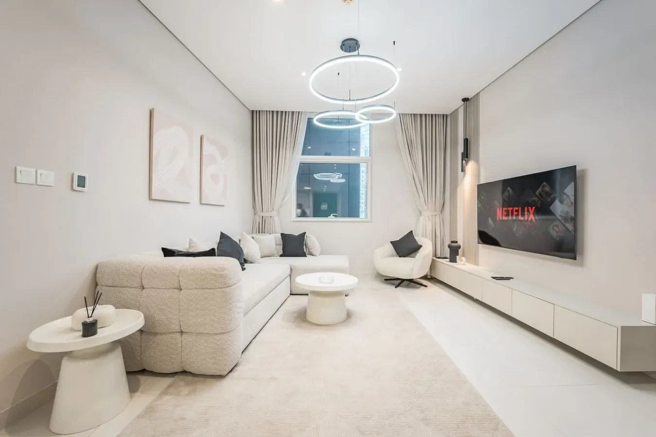 Una sala luminosa con asientos, un televisor y una gran ventana con cortinas.