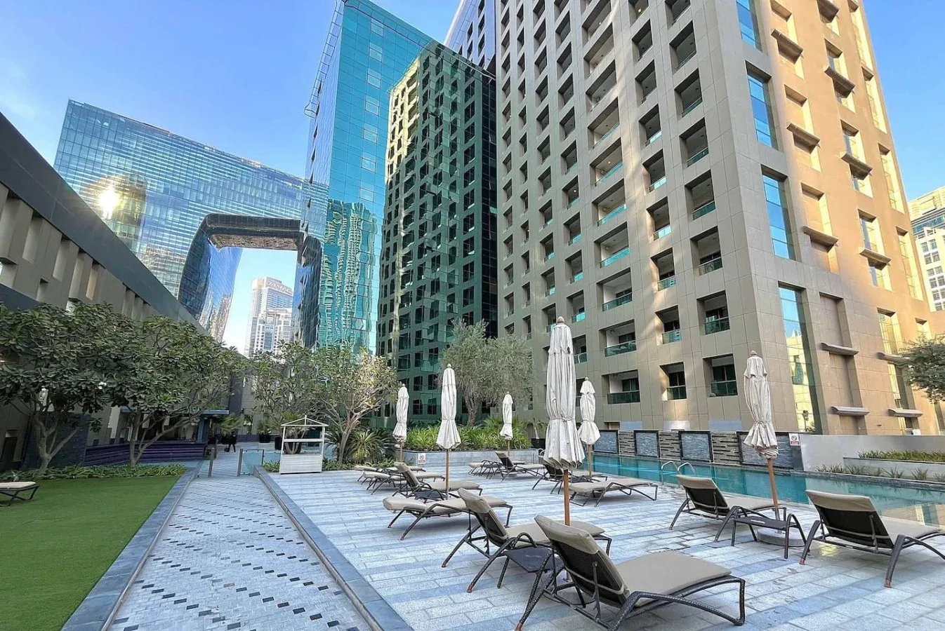 Una terraza de piscina al aire libre con tumbonas y sombrillas cerradas entre edificios altos.