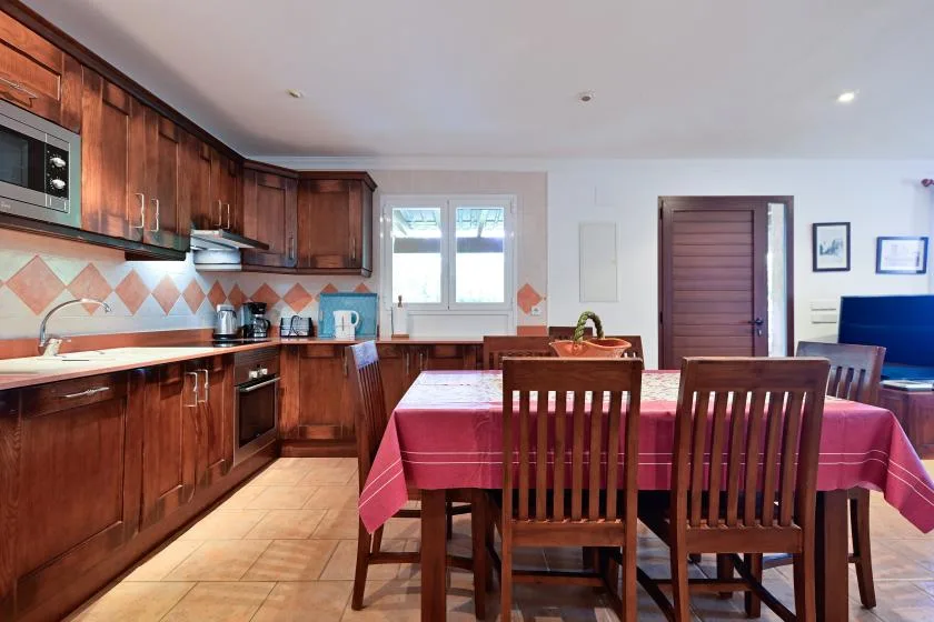 Una cocina y comedor con armarios de madera y una mesa cubierta con un mantel rojo.