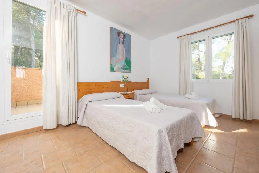 Un dormitorio luminoso con dos camas y ventanas enmarcadas por cortinas claras.