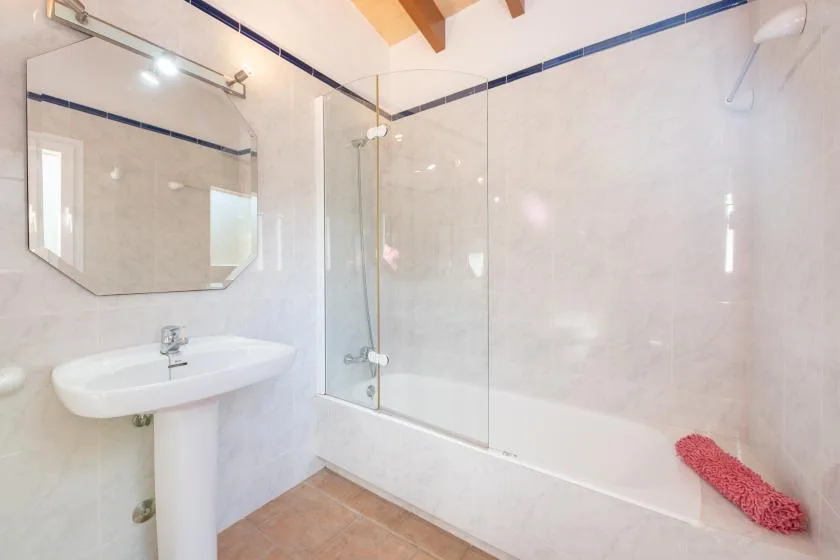 Un baño alicatado con lavabo de pedestal, espejo y bañera.
