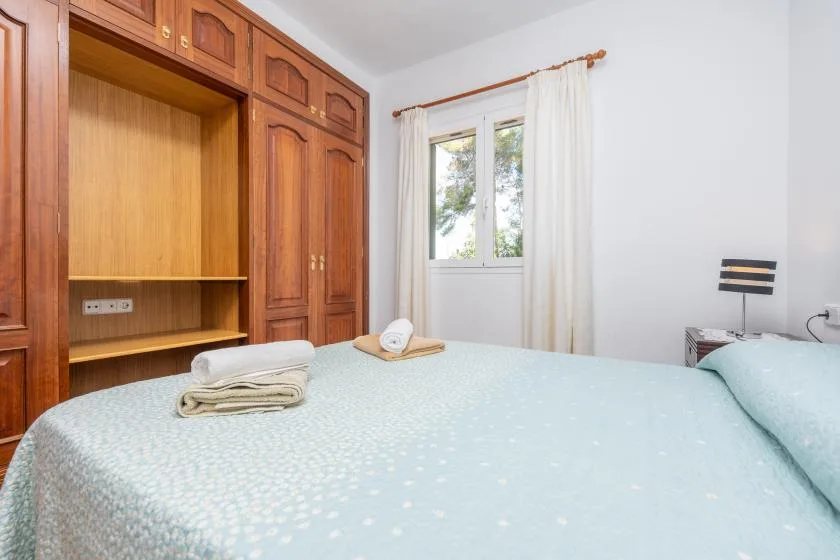 Un dormitorio con una cama, armarios de madera y una ventana con cortinas.