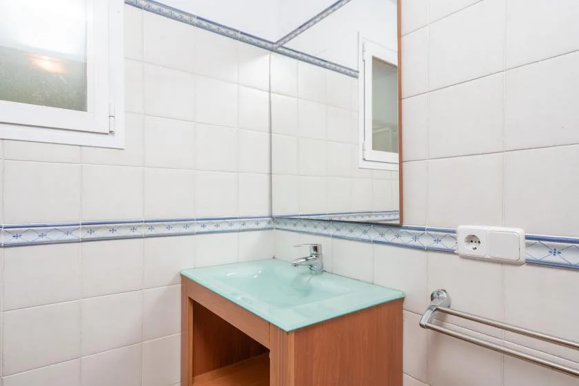 Un baño alicatado con un lavabo de encimera de vidrio y espejo de pared.