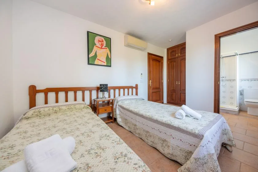 Un dormitorio con dos camas, una mesita de madera y una entrada al baño.