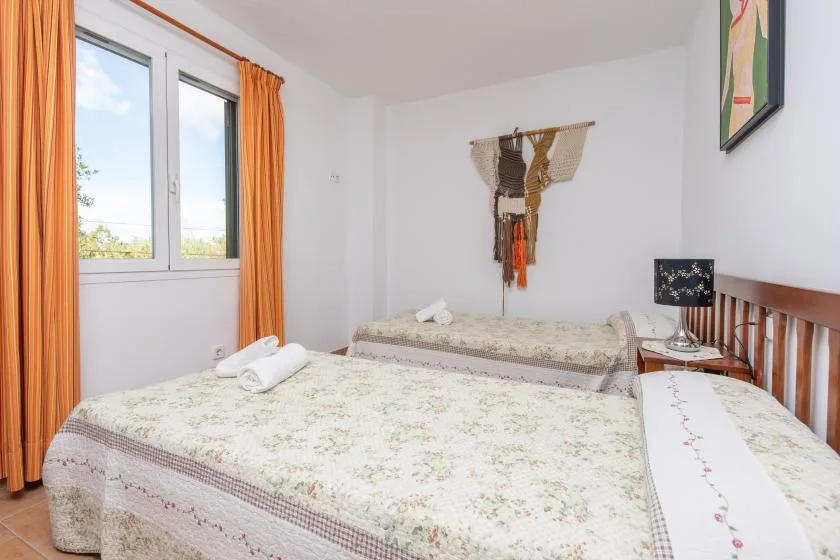 Un dormitorio con dos camas, cortinas naranjas y un tapiz en la pared.