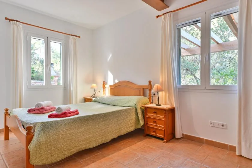 Un dormitorio con una cama de madera, mesitas de noche y dos ventanas.