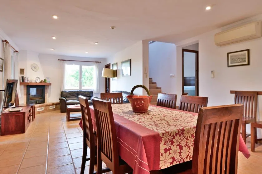 Un comedor con una mesa larga y asientos de madera, junto a una sala de estar.