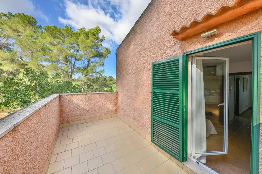 Una terraza exterior con baldosas junto a una puerta abierta con contraventanas verdes.