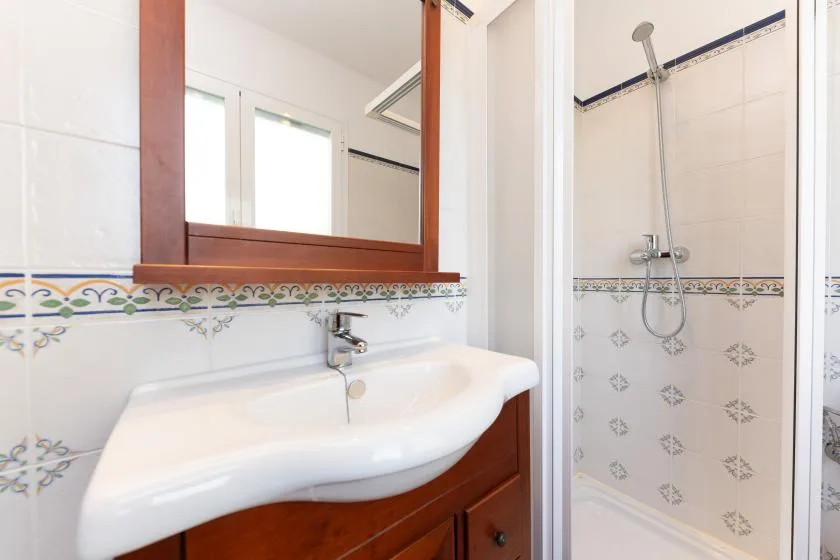 Un lavabo de baño con espejo está junto a una ducha alicatada.