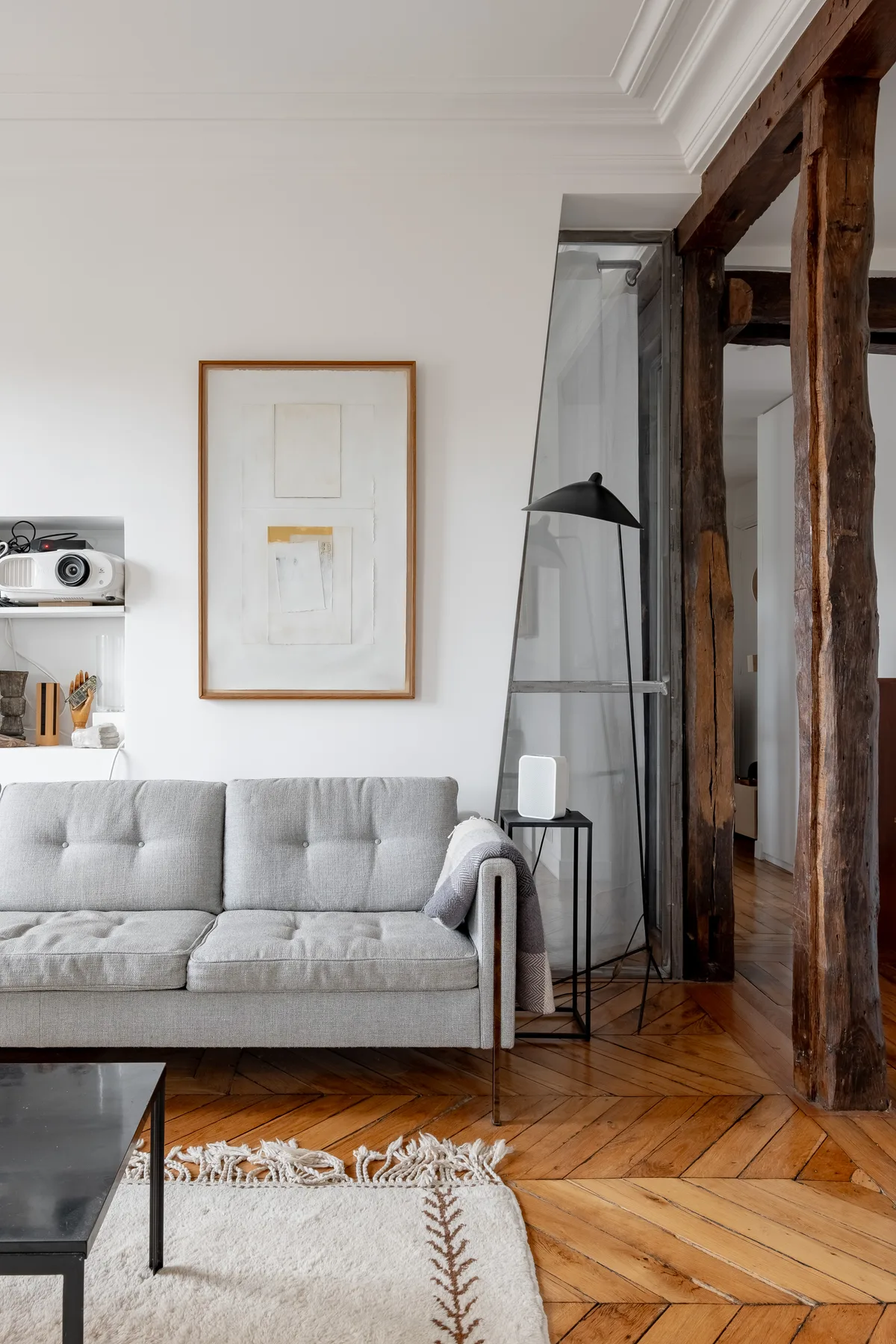 A bright living room with a gray sofa, framed artwork, and dark wooden beams.