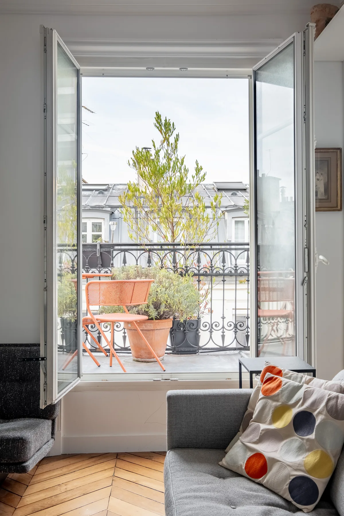 A bright sitting area opens onto a balcony with potted plants and outdoor seating.