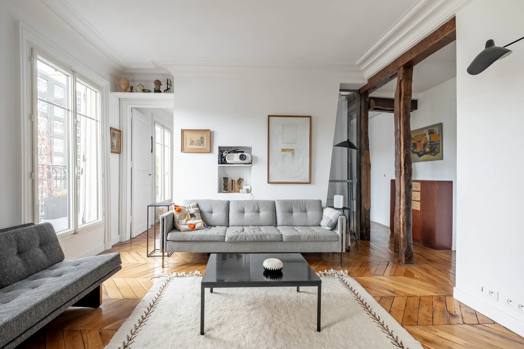 A bright living room with gray seating, a coffee table, and tall windows.