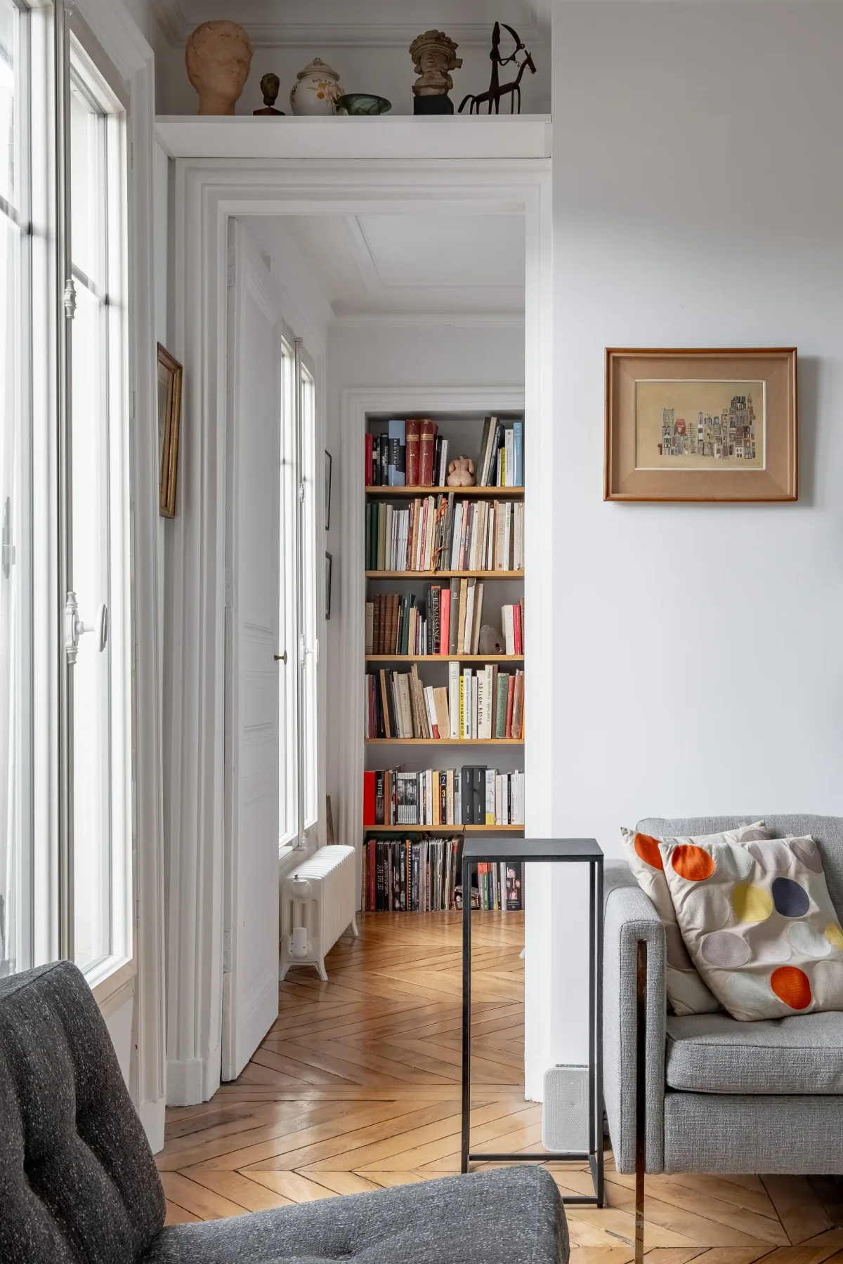 A bright living room opens onto a hallway lined with bookshelves.