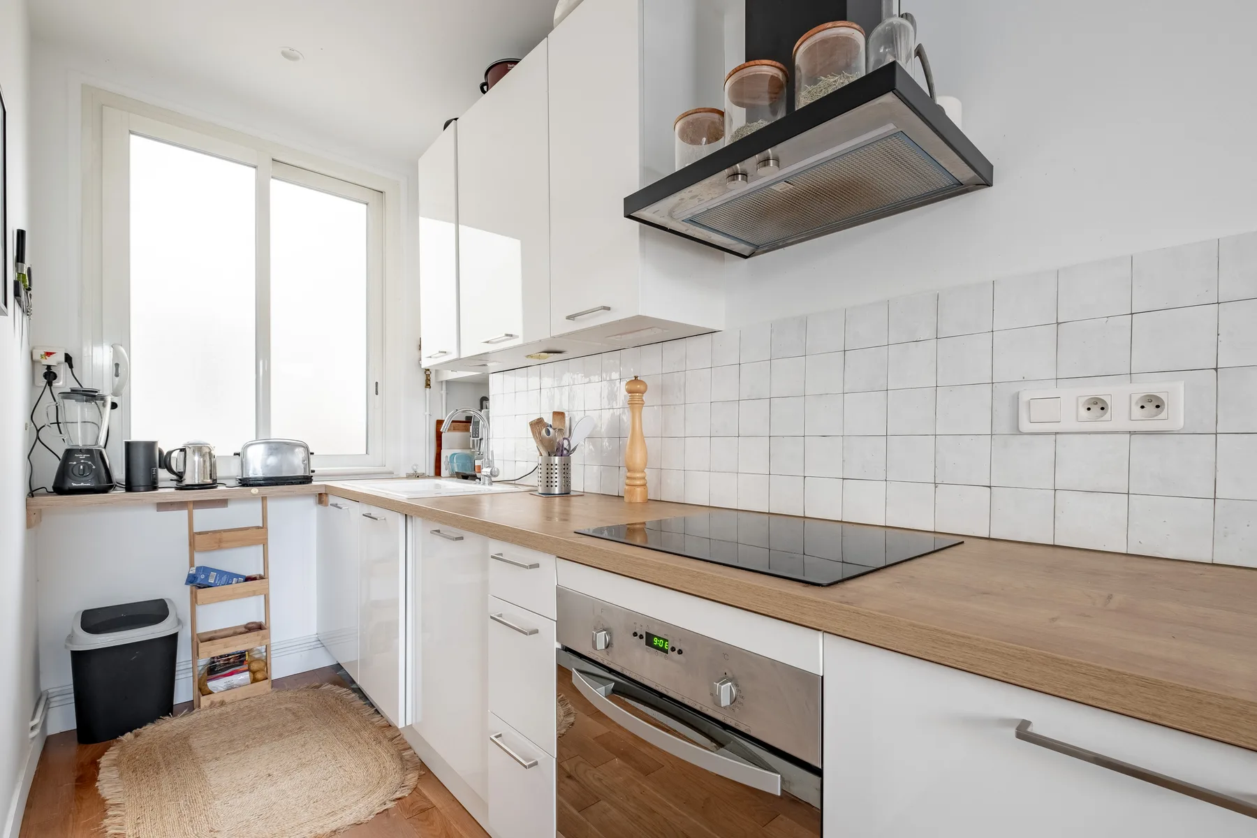 A bright kitchen with white cabinets, a wooden countertop, and a cooktop.