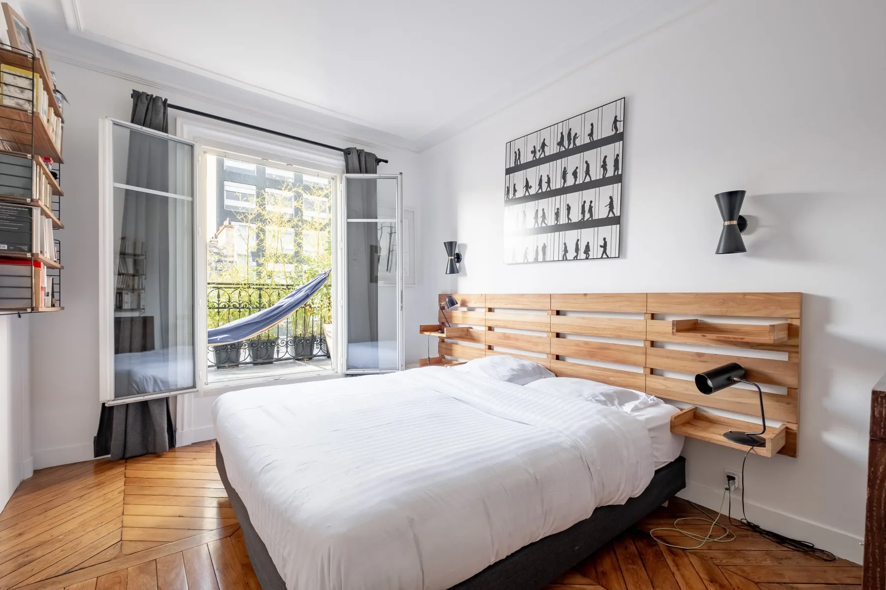 A bright bedroom with a bed, wooden headboard, and open balcony doors.