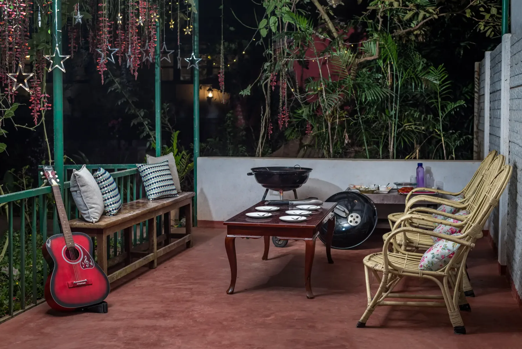 A covered patio has seating, a low table, and a guitar.