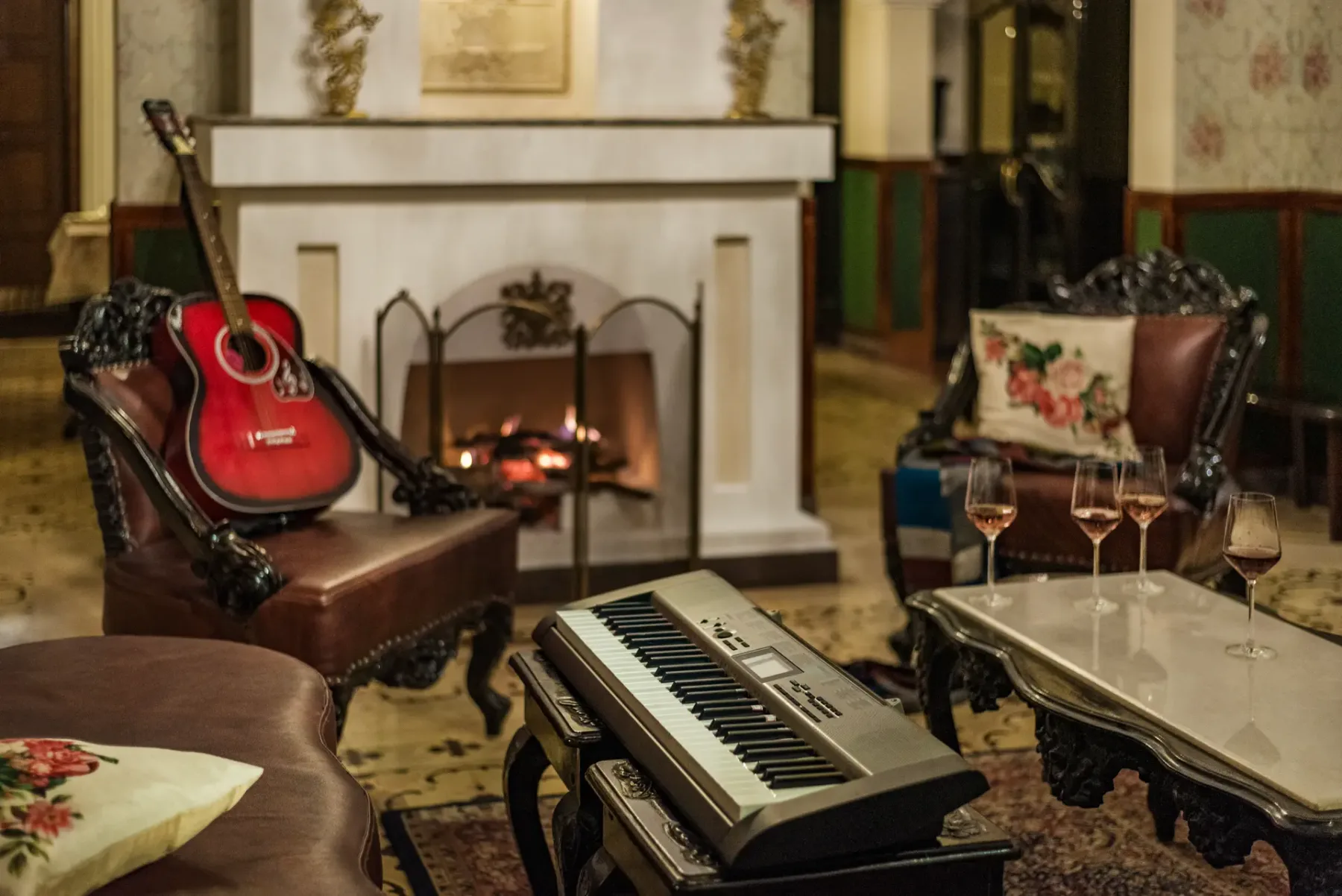 A sitting room with a lit fireplace, guitar, and keyboard.