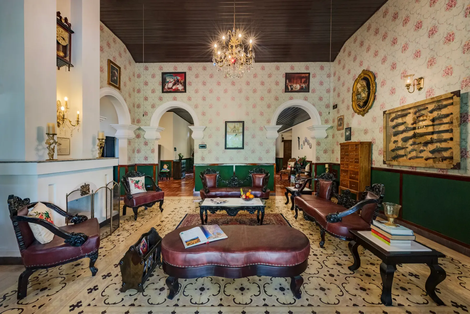 An ornate lounge with patterned wallpaper, seating, and a chandelier.