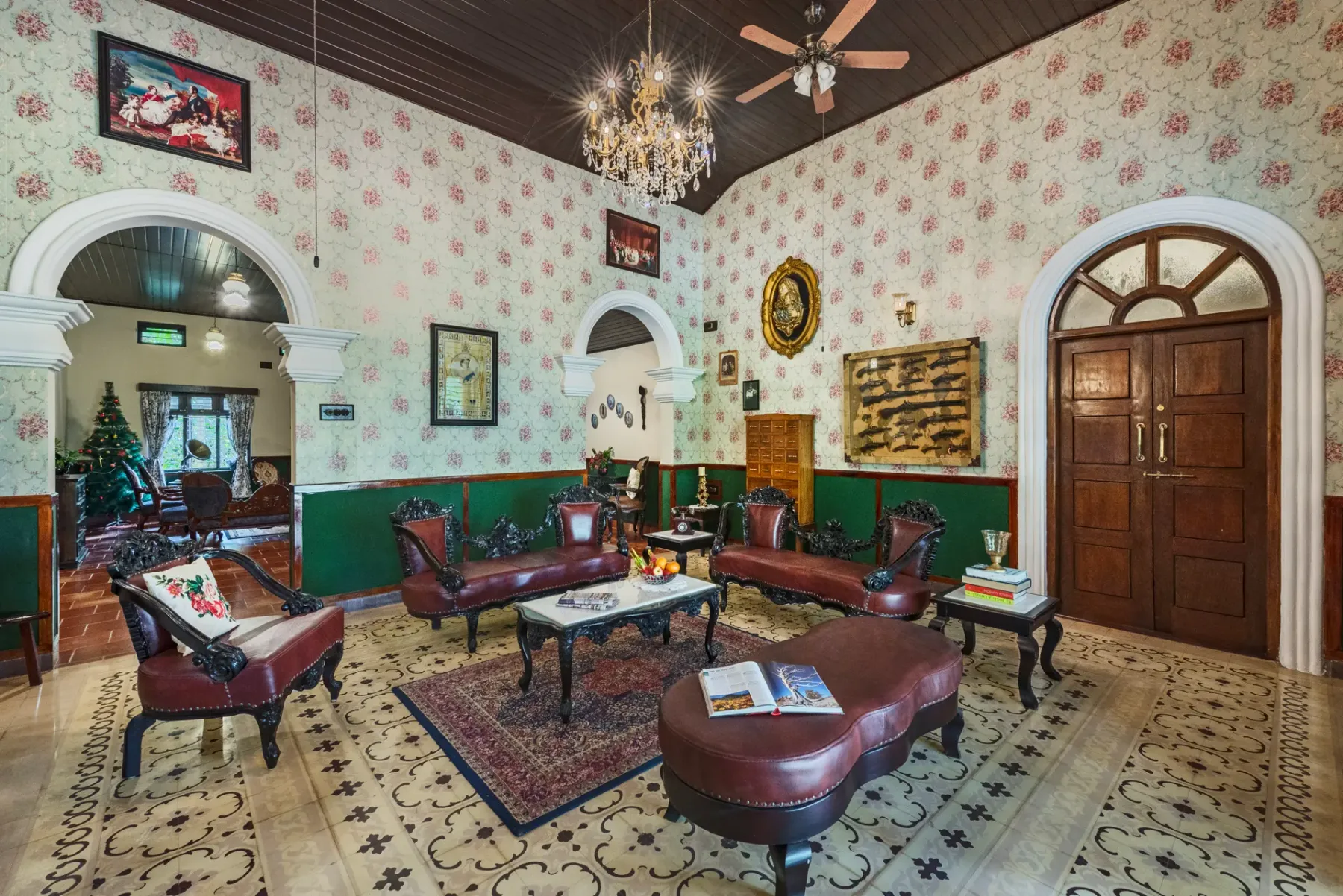 A sitting room with patterned wallpaper, dark seating, and a chandelier.