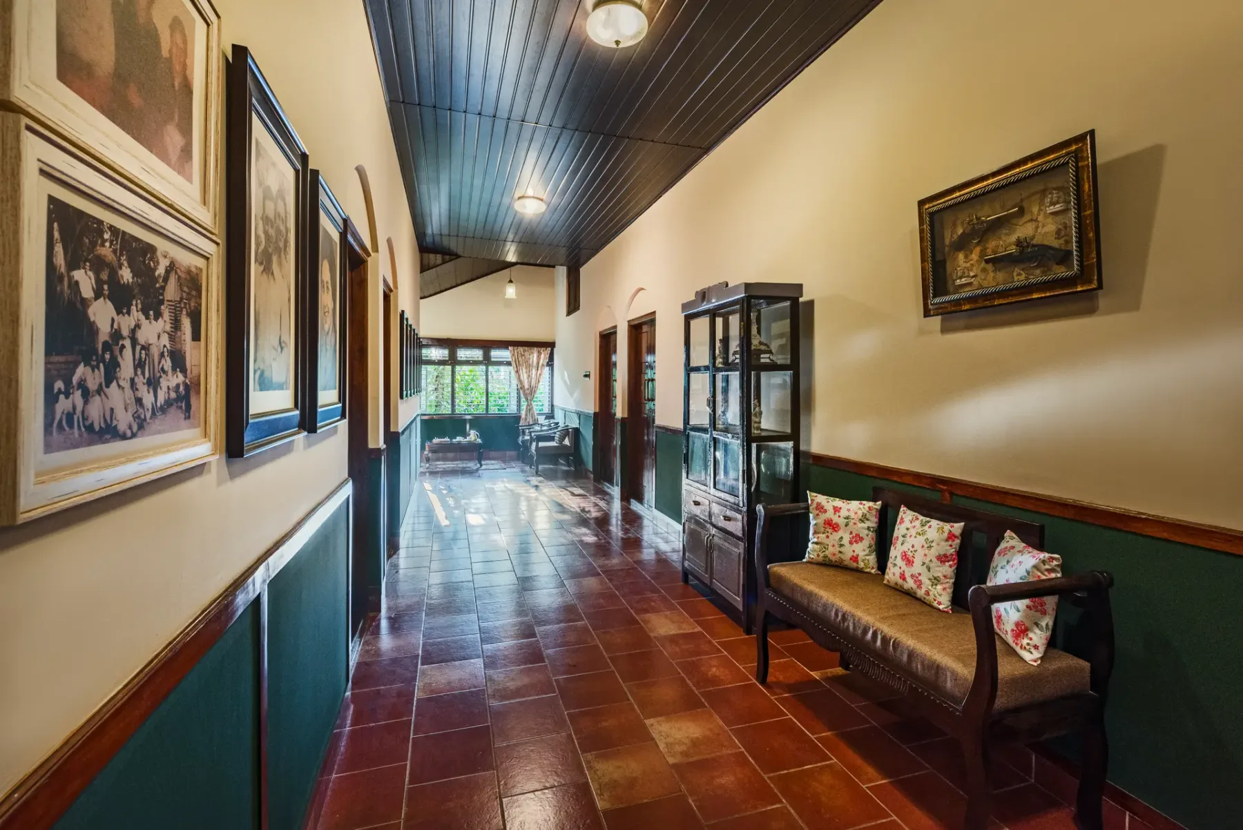 A long hallway with framed artwork, a glass cabinet, and a bench.
