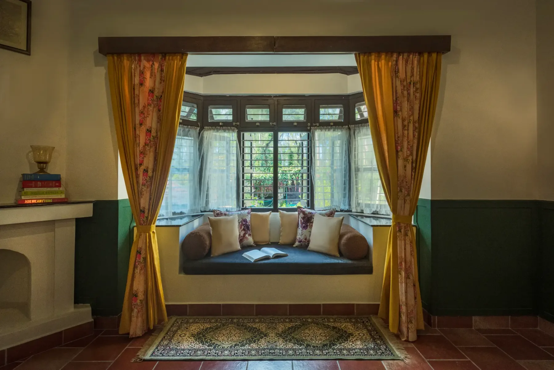 A window seat with cushions sits between patterned curtains in a bright room.