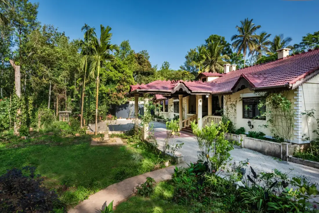 A single-story house with a red tiled roof sits among tropical greenery.