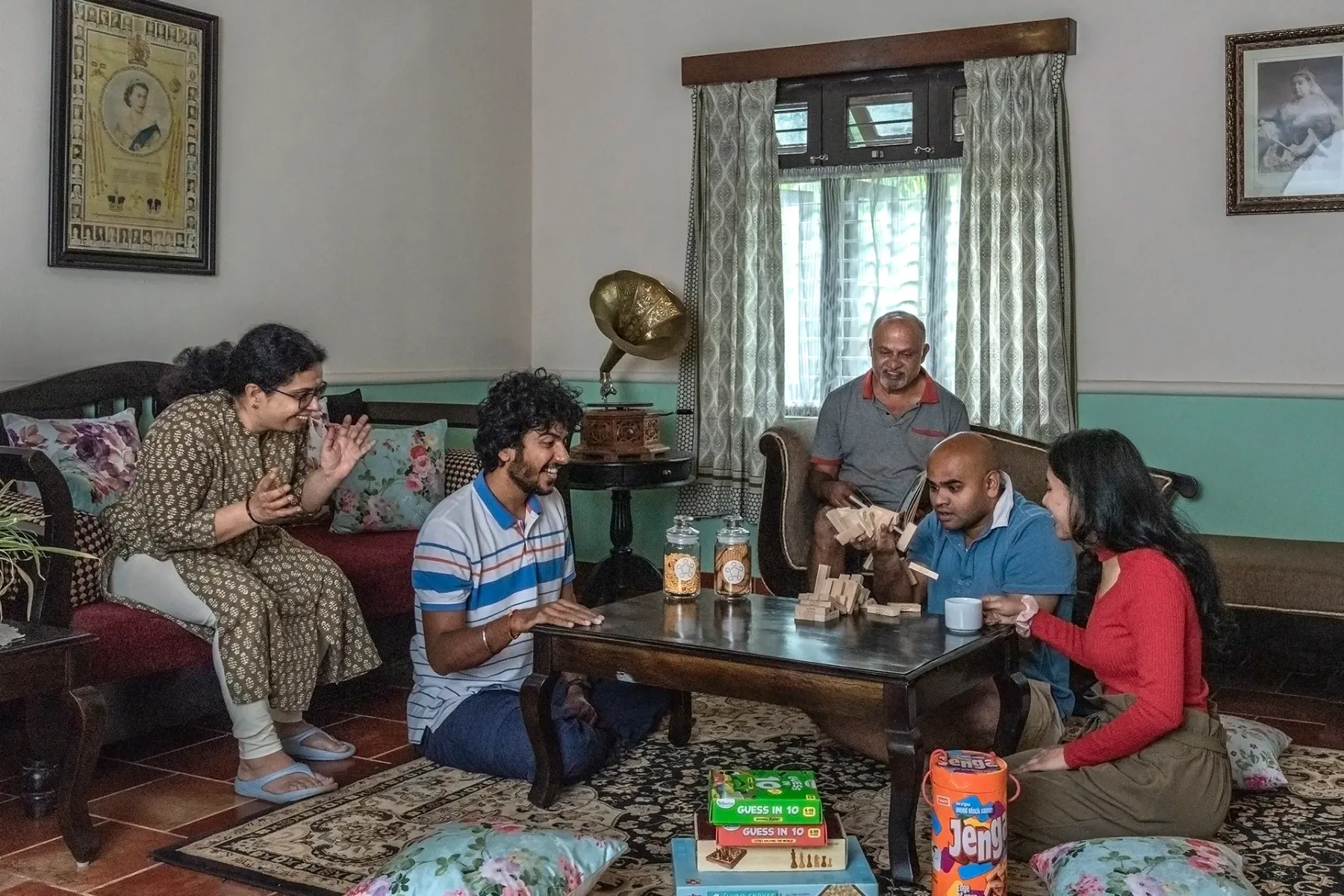 People gather around a low table in a living room with patterned seating.