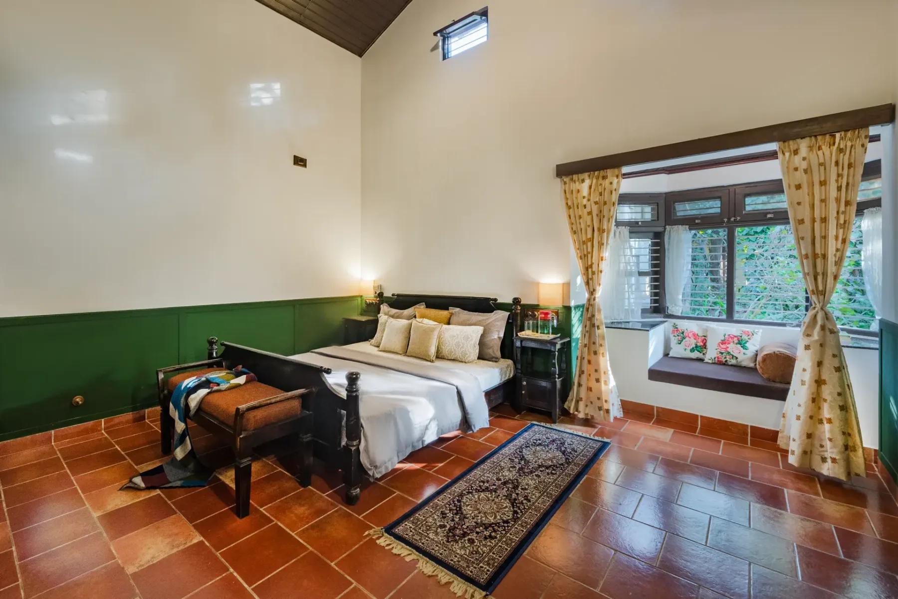 A bedroom with a large bed, patterned rug, and curtained window.