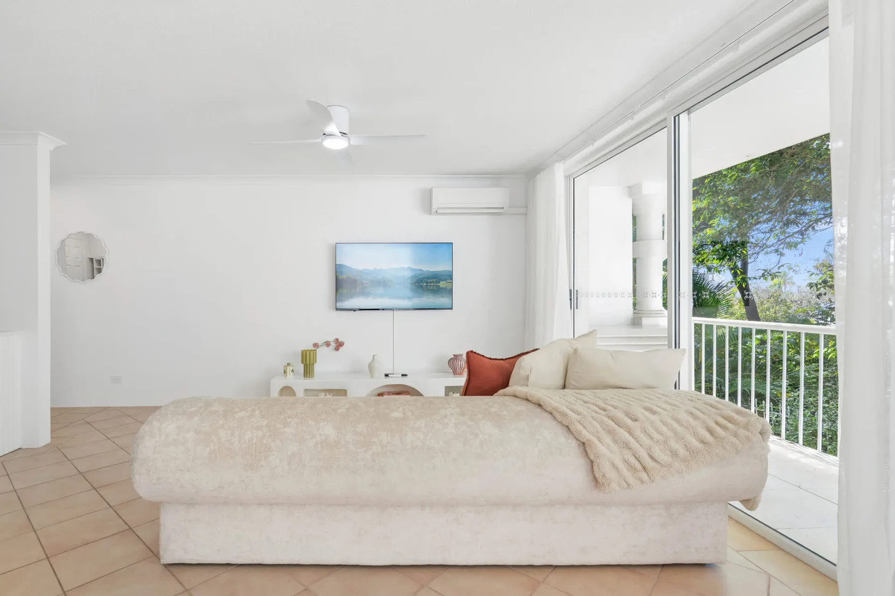 Un dormitorio luminoso con una cama grande junto a puertas corredizas de vidrio con vista a la vegetación.