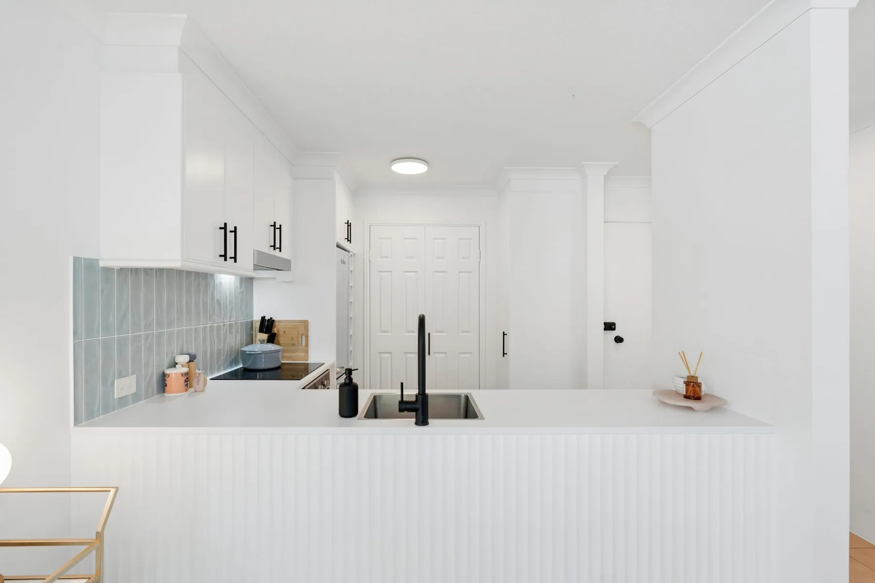 Una cocina blanca y luminosa con salpicadero de azulejos y una barra en primer plano.