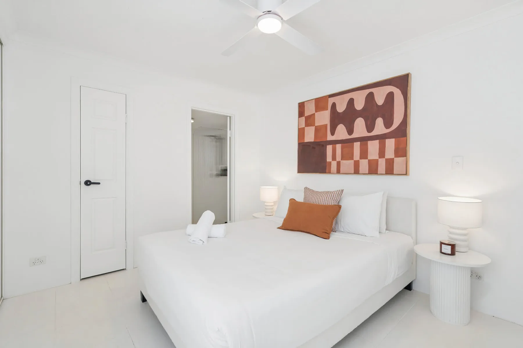 Un dormitorio luminoso con una cama blanca y arte abstracto en la pared.