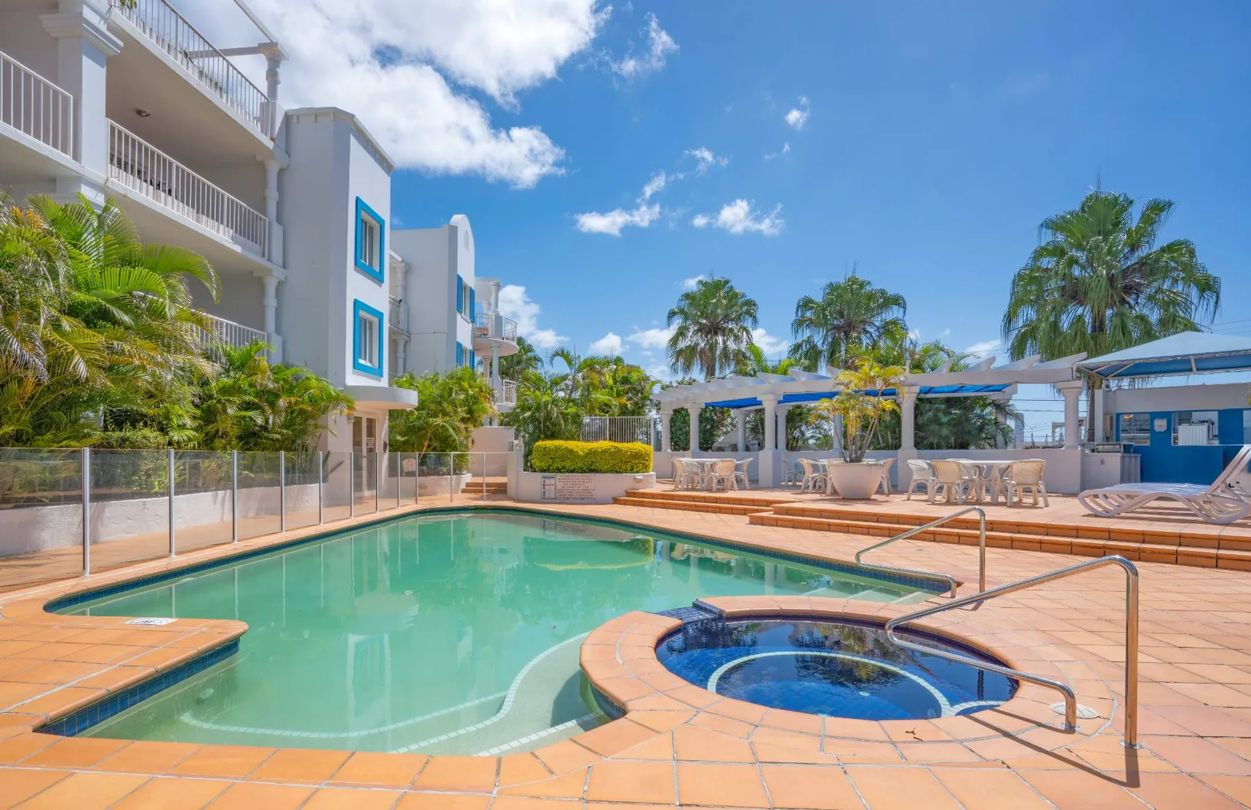 Una piscina al aire libre junto a una terraza pavimentada, una zona de estar y jardines.
